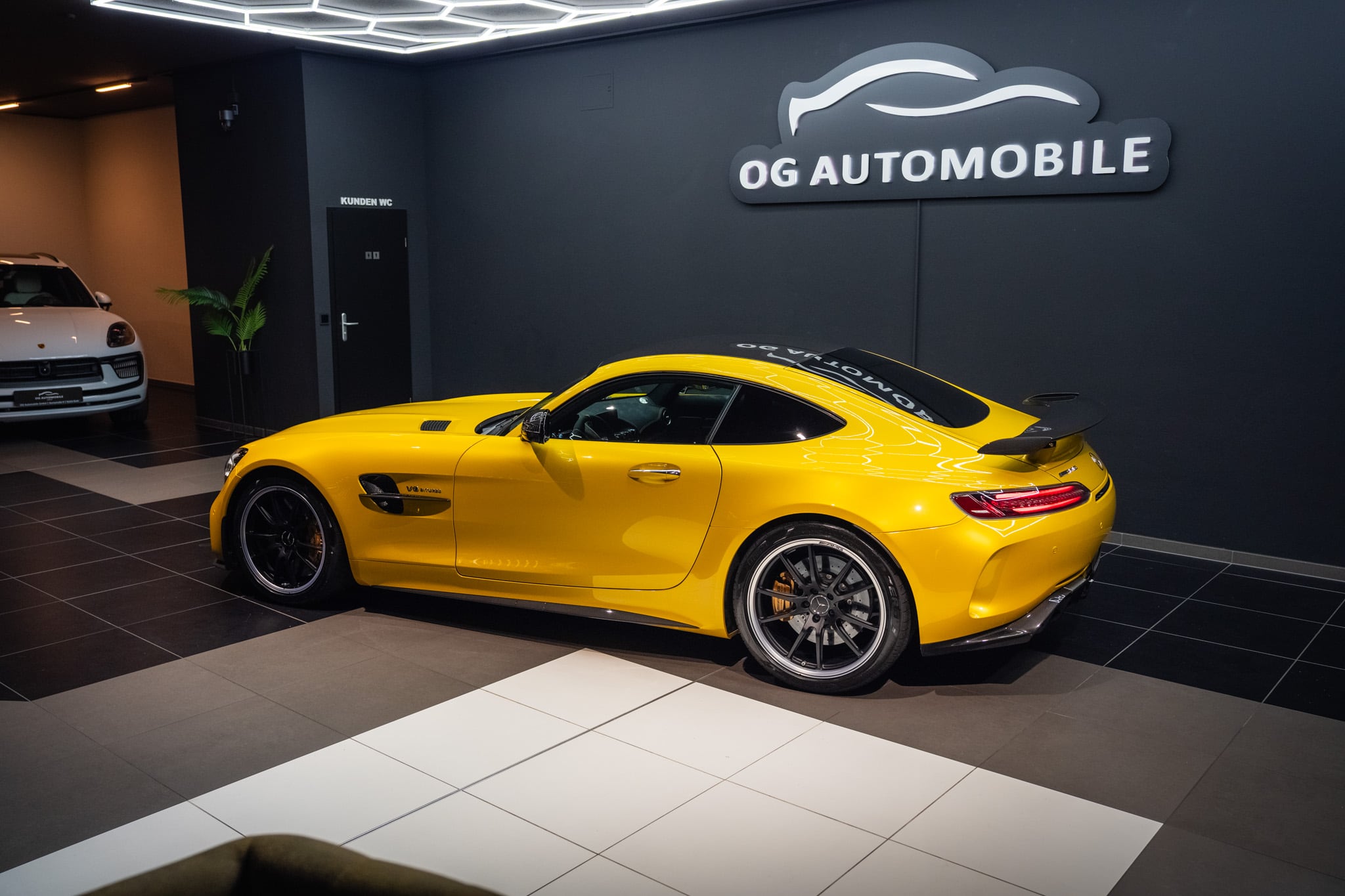 Gelber Mercedes-AMG GT R vor dem Logo der OG Automobile GmbH